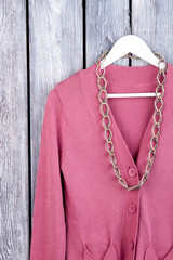 Chain necklace on pink coat, close up. Flat lay, top view. Dark wooden desk surface background.