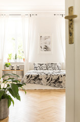 Opened door to a bedroom interior with a plant and double bed with floral sheets