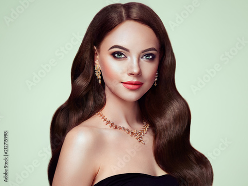 Brunette Girl with Long Healthy and Shiny Curly Hair. Care and Beauty. Beautiful Model Woman with Wavy Hairstyle. Make-Up and Jewelry