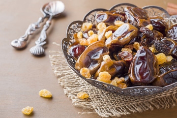 Oriental sweets, dried fruit dates and raisins, cinnamon and star anise in a plate on a wooden background.