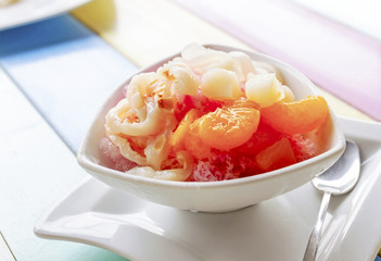 A bowl of fruits dessert with ice on colorful wooden table