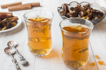 Oriental sweets, dried fruit dates and raisins, cinnamon and star anise in a plate. Turkish tea in glasses on a wooden background.
