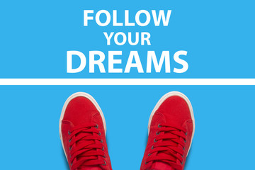 Female feet in red sneakers standing in front of the white line with the text Follow your dreams behind the line. Concept of obstacles to the achievements of desires. Flat lay, top view