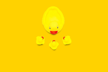 Rubber toy of yellow color Mama duck and small ducklings on a yellow background. The concept of maternal care and love for children. Flat lay, top view