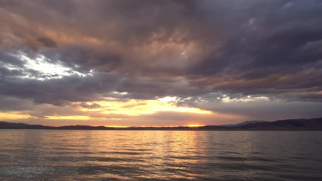 Colorful sunset reflecting in Utah Lake as the sun peaks through as it sets.