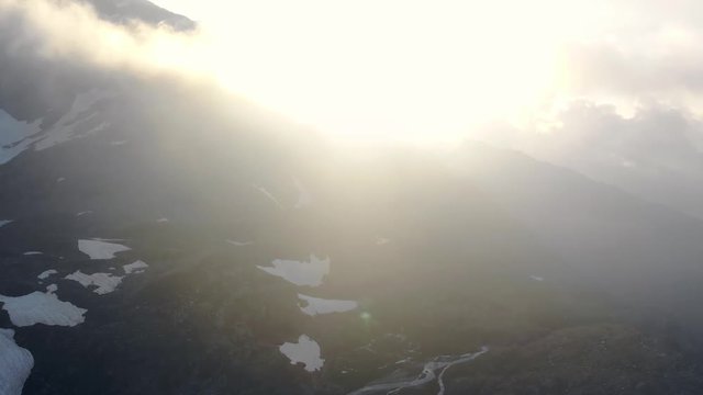 Aerial: flying over alpine valley at sunrise, high altitude mountain range in backlight with mountain hut