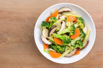 top view of stir fried vegetable with soy sauce in a ceramic dish on wooden table. homemade style food concept.