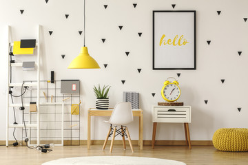 Yellow clock on cabinet next to white chair and desk in kid's room interior with lamp. Real photo