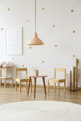 White round rug in bright child's room interior with lamp above table and wooden chairs. Real photo