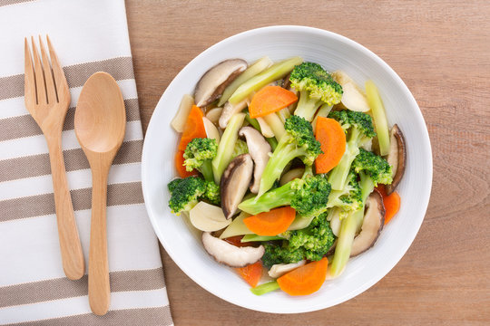 top view of stir fried vegetable with soy sauce in a ceramic dish on wooden table. homemade style food concept.