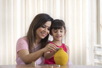 Fototapeta premium Mother and daughter filling piggy bank