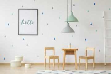 Lamps above wooden table and chairs in bright kid's room interior with poster on the wall. Real...