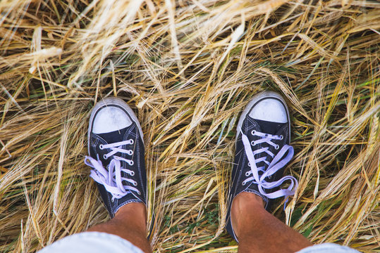 Man wearing black and white sneakers and standing in golden barley field.