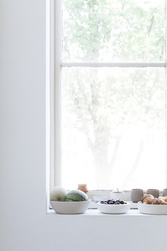 A window sill in a clean and white interior has been set up with a lot of summer fruit and some croissants.
