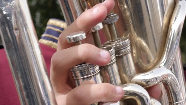 Extreme close up of hand pressing buttons of a tuba during an outdoor marching band performance