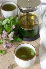 Mint tea in a clear glass teapot, mint leaves and tea cups.