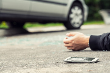 Broken phone next to a hand of a victim lying on the street