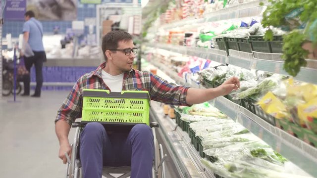 Man with a disability in a wheelchair chooses the goods in the shopping in the supermarket close up