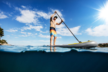 Young man on paddleboard, half under and half above water composition