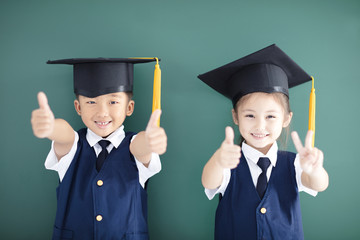 Happy boy and girl in graduation cap showing thumbs up - Powered by Adobe