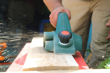 Work tool. A carpenter man is laying a wooden plank against an electric plane. Processing of wood...