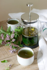 Mint tea in a clear glass teapot, mint leaves and tea cups.