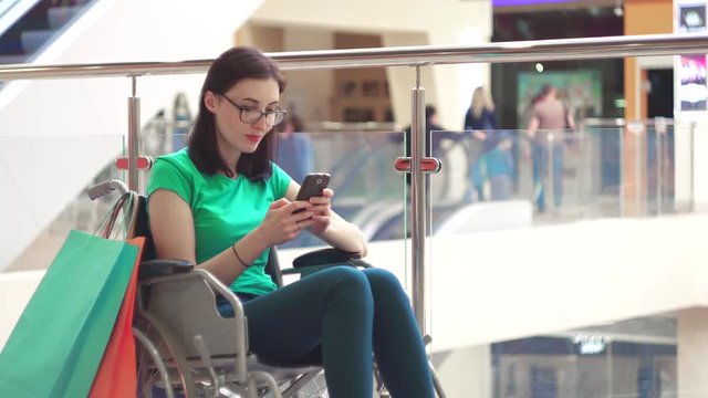 A woman with a disability in a wheelchair uses the phone at the Mall after shopping.Close up