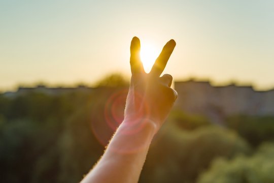 Hand showing two fingers or victory gesture. Background evening sunset, city silhouette