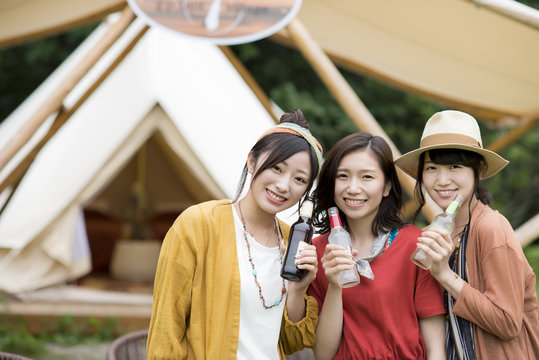 グランピングテントの前で飲み物を持ち微笑む若者たち