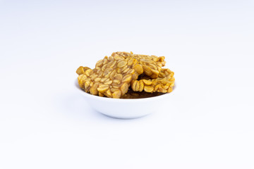 Fried tempeh or soybean cake in white bowl over a white background. It is made by fermentation process that binds soybeans into a cake form.
