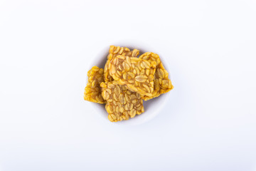 Fried tempeh or soybean cake in white bowl over a white background. It is made by fermentation process that binds soybeans into a cake form.