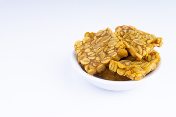 Fried tempeh or soybean cake in white bowl over a white background. It is made by fermentation process that binds soybeans into a cake form.