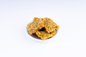 Fried tempeh or soybean cake in white bowl over a white background. It is made by fermentation process that binds soybeans into a cake form.