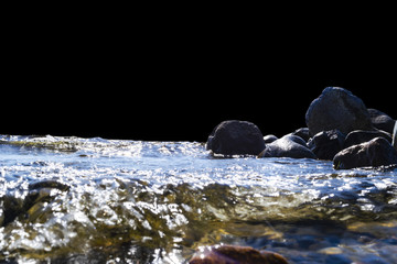 Big windy waves splashing over rocks. Wave splash in the lake isolated on black background. Waves breaking on a stony beach, forming a spray. Water splashes. Water surface texture