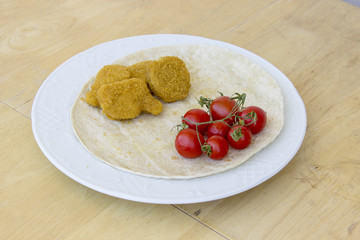 Beautiful perspective shot of chicken nuggets and small red fresh tomatoes on the wide white plate as a breakfast with thin bread