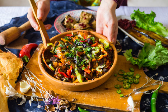 Woman hands holds ajapsandal vegetables stew in clay ketsi dish. Traditional Georgian food cooked with different sorts of seasonal vegetables and greens (meat as option). Caucasus lunch or dinner. 