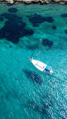 Aerial drone birds eye view of sail boat docked in an Ionian island with crystal clear emerald sea, Greece