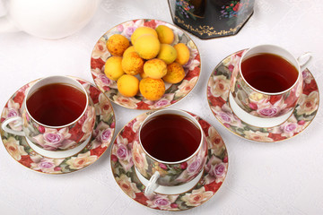 Three full porcelain teacups with floral pattern, box with tea, teapot and plate with wild apricots