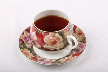 Single full porcelain teacup with hot tea and with floral pattern on a white cloth