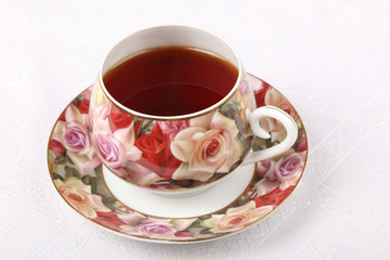 Single full porcelain teacup with hot tea and with floral pattern on a white cloth