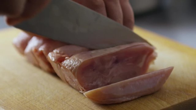 Close-up of male hands cutting chicken fillet with knife on wooden board on kitchen table