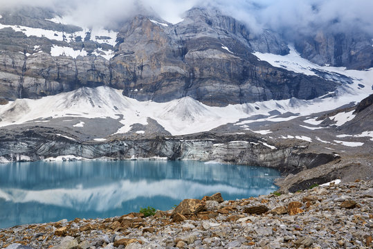 Griessee (auch Gletscherseeli genannt) unterhalb des Claridengletschers, Wasserspiegelung, Clariden Nordwand, Nebel, im Vordergrund goldfarbene Gesteinsformationen