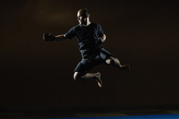 Fototapeta na wymiar In a black T-shirt, an athlete trains a jump for a punch hand