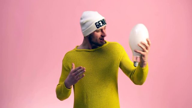 The guy in a yellow sweater and a white cap keeps a dialogue with a light bulb held in his hand. Concept of the emergence of the idea.