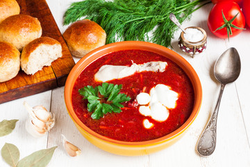 A bowl of homemade red borscht with sour cream and freshly baked garlic buns close-up. Tasty and healthy beetroot soup