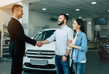 Obraz premium Young modern happy couple buying a new car in city dealership and talking with salesman