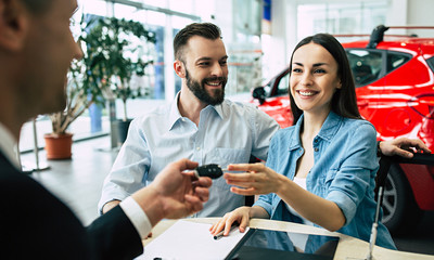 Beautiful happy couple bought a car in the dealership and receives the keys from the manager.