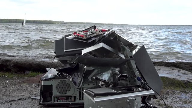 Broken computer parts, monitors and printers in front of nature landscape with a river background. Discarded electronic appliances free standing in nature. Computer parts. Broken computer on ground