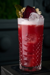 Red cocktail with foam, beet and mint in a cold glass on the bar in a black background