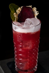 Red cocktail with foam, beet and mint in a cold glass on the bar in a black background